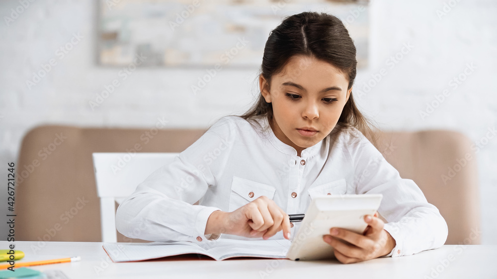 Preteen girl using calculator near notebook and stationery at home.