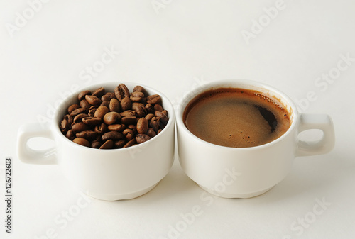 Coffee beans and espresso in two white cups on white background