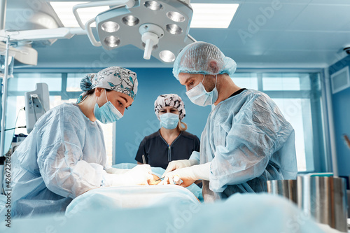 Doctors performing abdominoplasty surgery in the hospital. Focus on male plastic surgeon doing abdominal plastic surgery in operating room. Concept of tummy tuck and cosmetic surgery. photo
