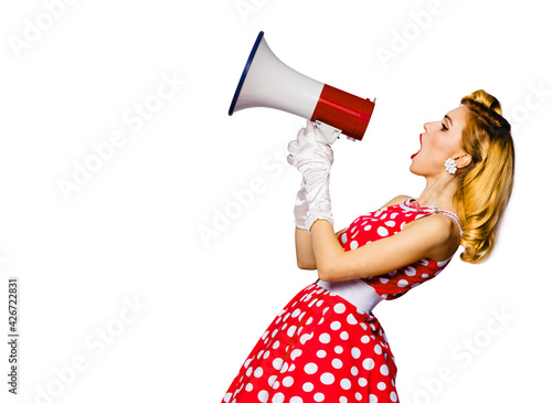 Beauty blond haired woman holding megaphone, shout something. Girl in pin up style red dress in polka dot isolated over white background. Caucasian model in retro fashion vintage advertising concept. photo