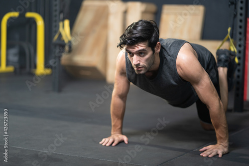 Handsome adult Caucasian men push up with trx robe to do crossfit exercise inside of fitness gym to workout for firm abs muscle and good body health.