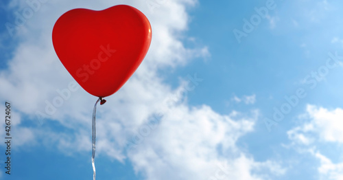 red heart-shaped balloon on blue sky background with clouds
