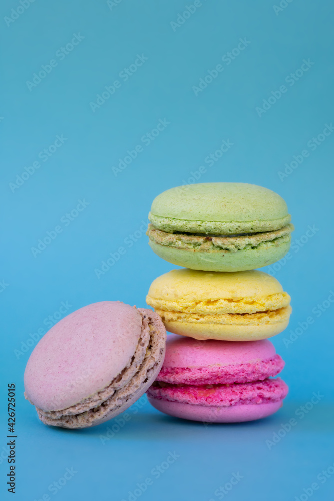 Vertical photo of group different colored french macarons on blue background. French dessert