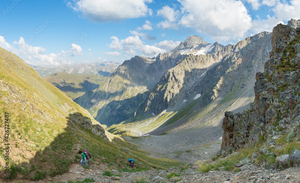 Fototapeta premium Very steep climb to the pass . Tourists climb up . Beautiful valley . Blue sky .