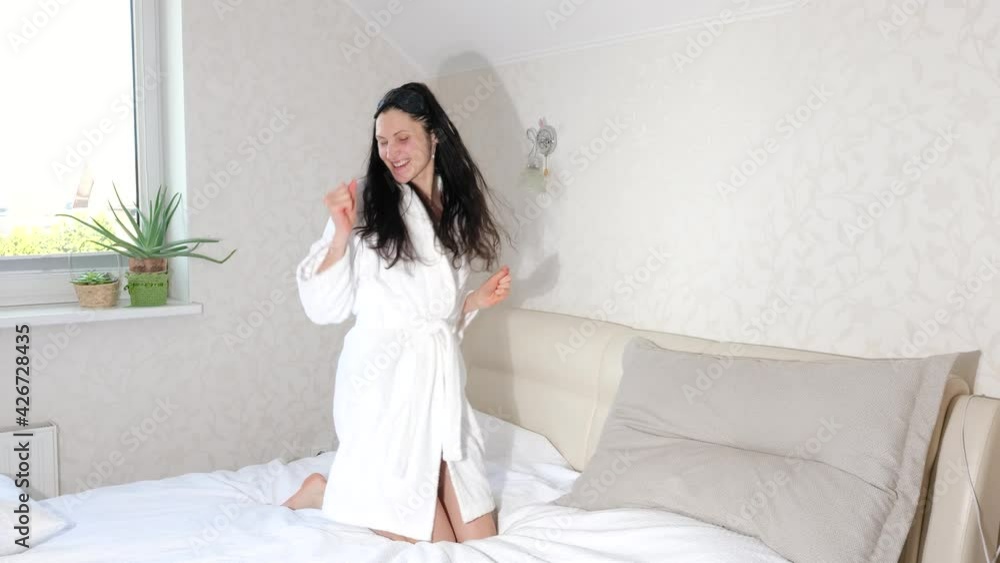 Happy young woman in bathrobe dances and jumps on white bed, happy morning time, 4K Happy young woman in bathrobe dances and jumps on white bed, happy morning time, 4K