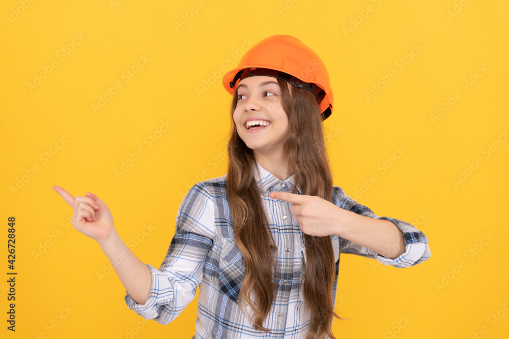 happy teen girl in helmet and checkered shirt pointing finger on copy space, advert