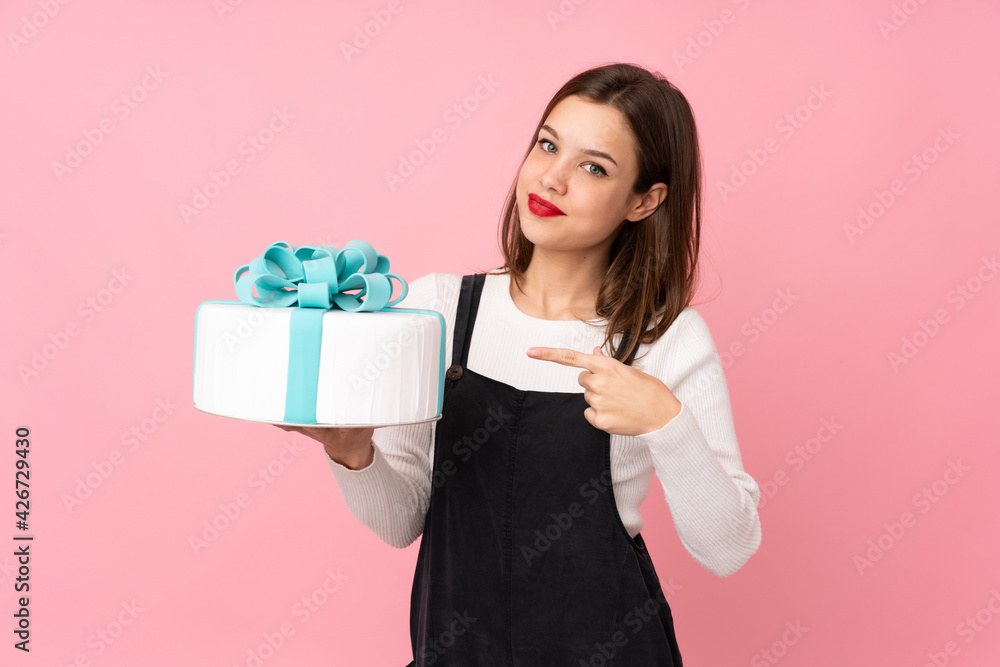 Girl holding a big cake isolated on pink background and pointing it Girl holding a big cake isolated on pink background and pointing it