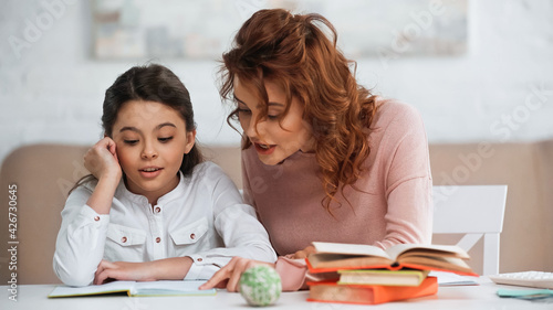 Woman talking to daughter while helping with homework near books.