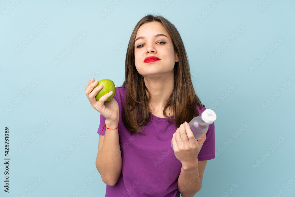 Teenager girl isolated on blue background with an apple and with a bottle of water Teenager girl isolated on blue background with an apple and with a bottle of water