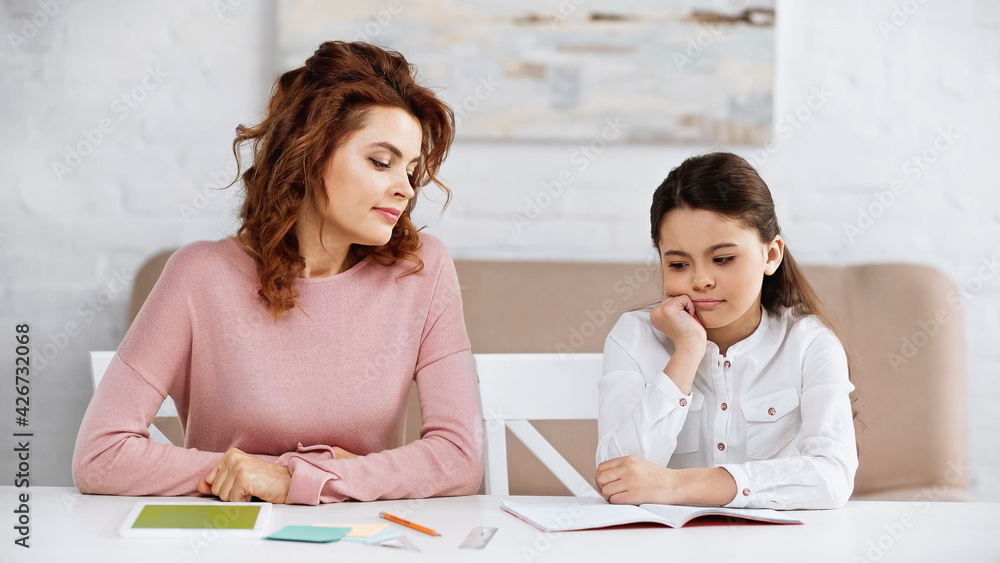 Woman sitting near kid and digital tablet during home education. Woman sitting near kid and digital tablet during home education.