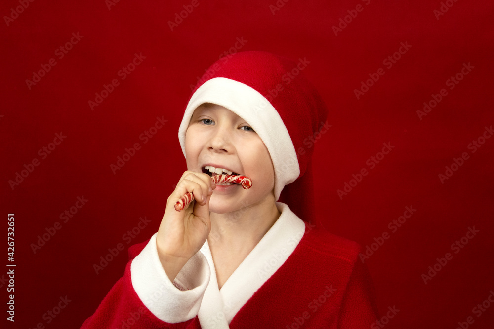 a boy in a red Santa Claus costume holds candy canes in his hands. a boy in a red Santa Claus costume holds candy canes in his hands.
