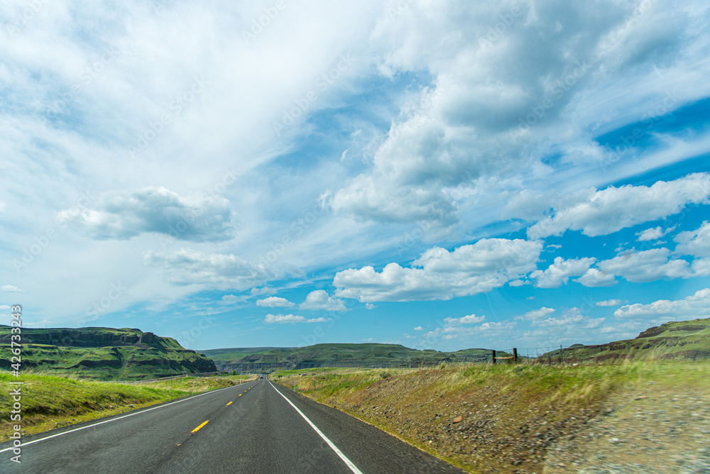 Travel-A Two-Lane Blacktop Road Approaching the Green-Carpeted Basalt Cliffs of the Columbia River Basin in Eastern Washington State Travel-A Two-Lane Blacktop Road Approaching the Green-Carpeted Basalt Cliffs of the Columbia River Basin in Eastern Washington State
