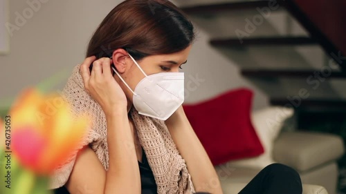 Young Woman putting on KN95 facemask and securing face mask kn-95 safely at home in her living room accommodating surgical facial mask by covering her face in pandemic times of coronavirus COVID 19 photo