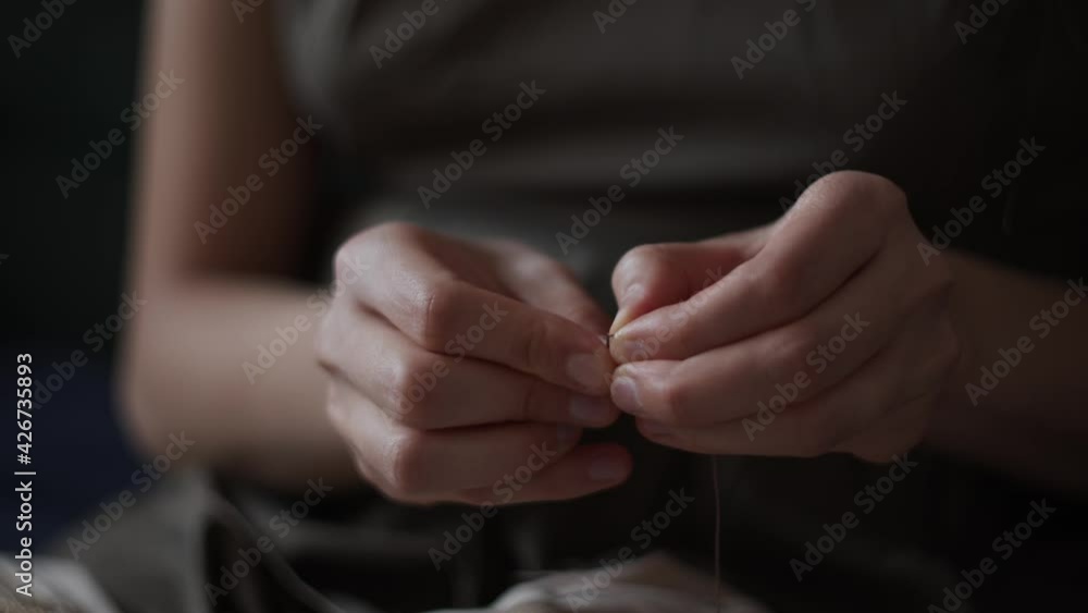 4K Close-up view of female hands inserting a thread into a needle hole for sewing. Young woman in green dress doing needlework. Hand made concept. Daylight. 4K Close-up view of female hands inserting a thread into a needle hole for sewing. Young woman in green dress doing needlework. Hand made concept. Daylight.