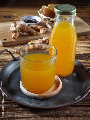 Jamu kunir asem or kunyit asam is Indonesian traditional herbal drink made from turmeric, tamarind, palm sugar. Served on tray with ingredients as background. Better served cold. Healthy refreshment. photo