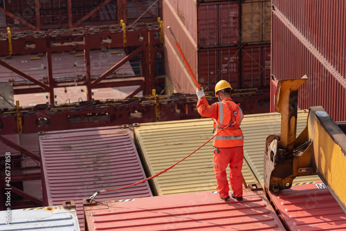 Asian foreman, port worker, assisting with unloading containers from cargo ship.
