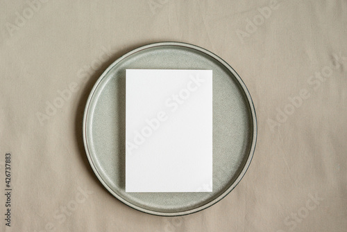 Blank greeting card mockup on ceramic plate and pastel textile background.