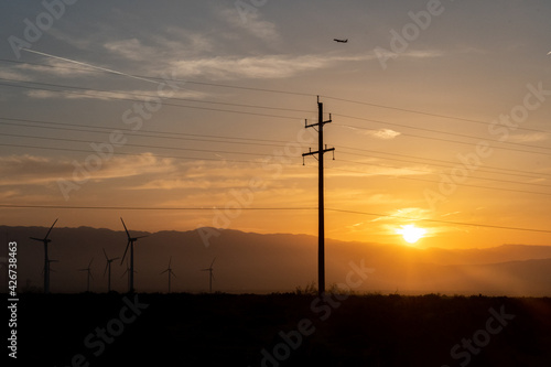 Sunrise in the desert with power lines and wind turbines.
