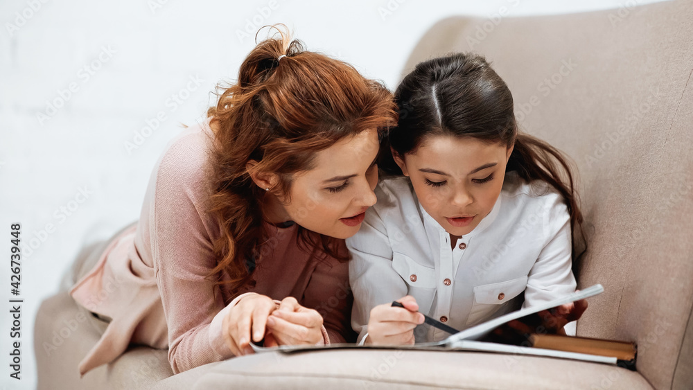 Woman lying near daughter doing homework and laptop on couch. Woman lying near daughter doing homework and laptop on couch.