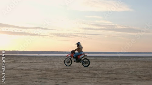 A girl motocross motorcyclist rides along a wide sandy beach against the backdrop of the setting sun. photo