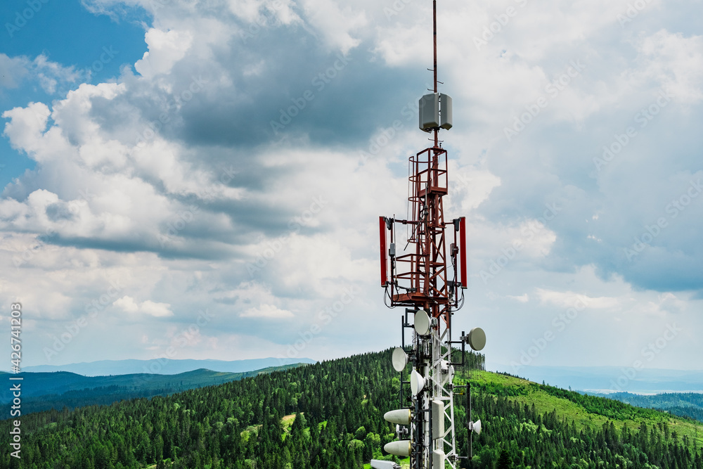 Telecommunication transmitter tower with antennas of cellular communication in mountains against sky and clouds