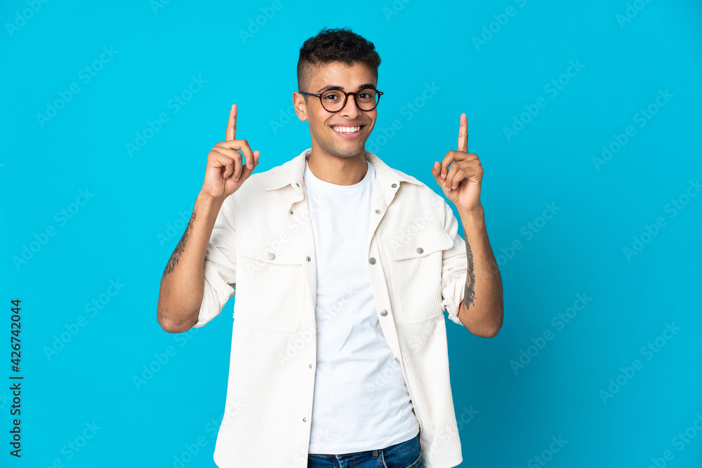 Young Brazilian man isolated on blue background pointing up a great idea Young Brazilian man isolated on blue background pointing up a great idea