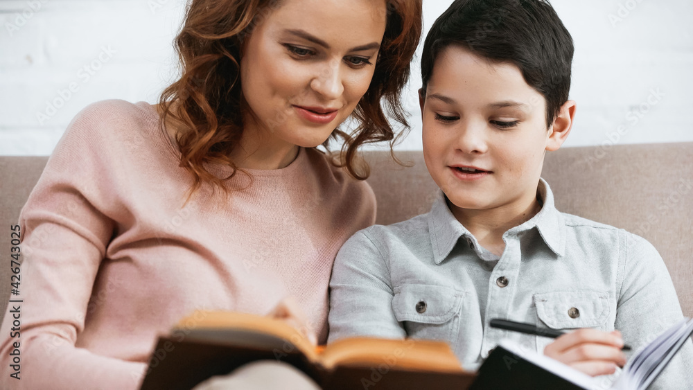Smiling woman reading book on blurred foreground with son. Smiling woman reading book on blurred foreground with son.