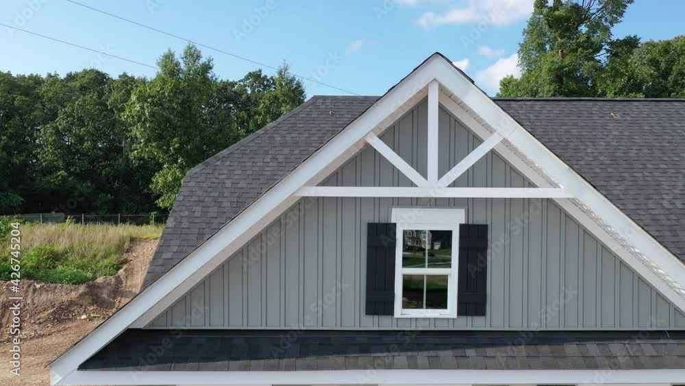 Horizontal flight along a triangle shape decorative gable with colonial white soffit and fascia on a gray horizontal vinyl siding modern American estate home with cloudy blue sky Horizontal flight along a triangle shape decorative gable with colonial white soffit and fascia on a gray horizontal vinyl siding modern American estate home with cloudy blue sky