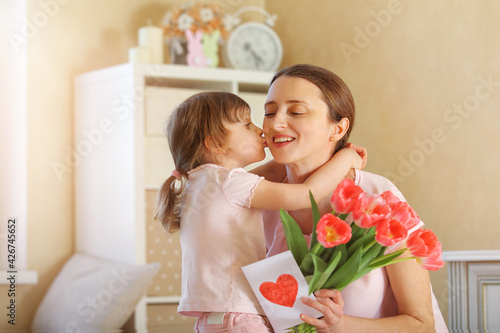 Happy Mother's Day. The child daughter congratulates her mother and gives her a homemade card and flowers pink tulips