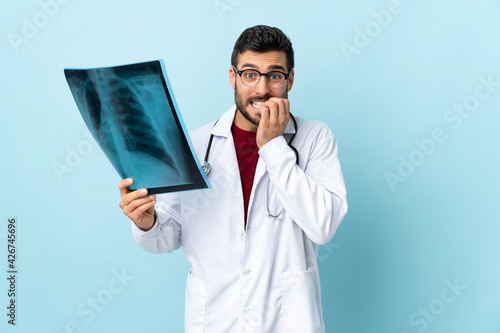 Professional traumatologist holding radiography isolated on blue background nervous and scared © luismolinero
