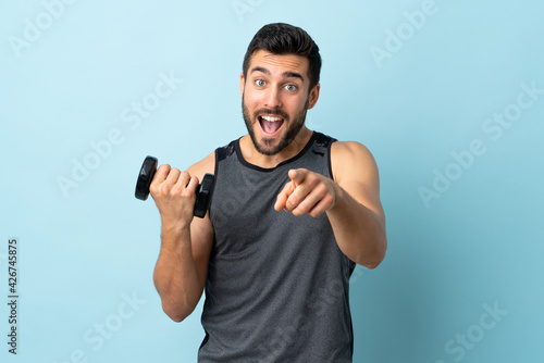 Young sport man with beard making weightlifting points finger at you with a confident expression