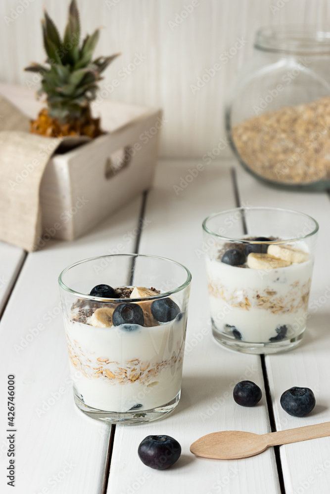 Two glasses with layered yogurt, oats and fruits, on white wooden table. Healthy breakfast, healthy lifestyle concept Two glasses with layered yogurt, oats and fruits, on white wooden table. Healthy breakfast, healthy lifestyle concept