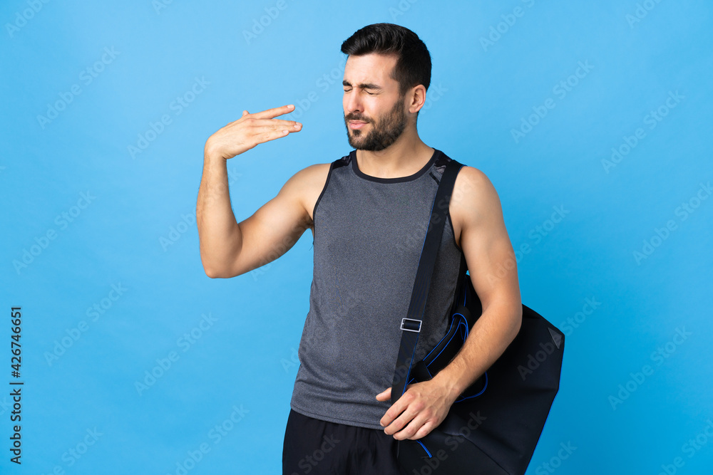 Fototapeta premium Young sport man with sport bag isolated on blue background with tired and sick expression