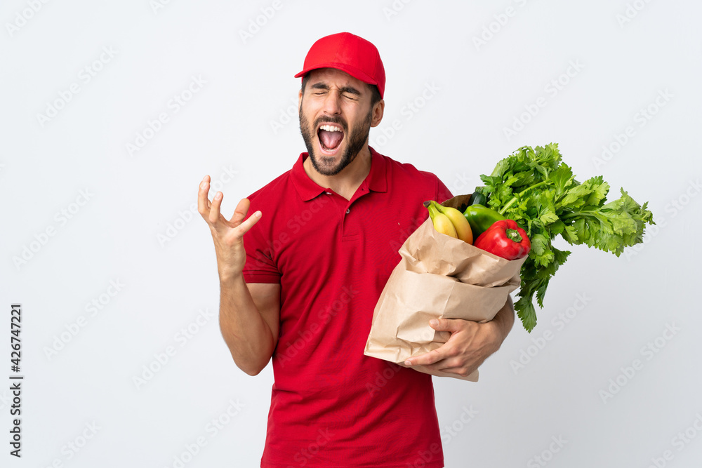Young man with beard holding a bag full of vegetables isolated on white background unhappy and frustrated with something Young man with beard holding a bag full of vegetables isolated on white background unhappy and frustrated with something