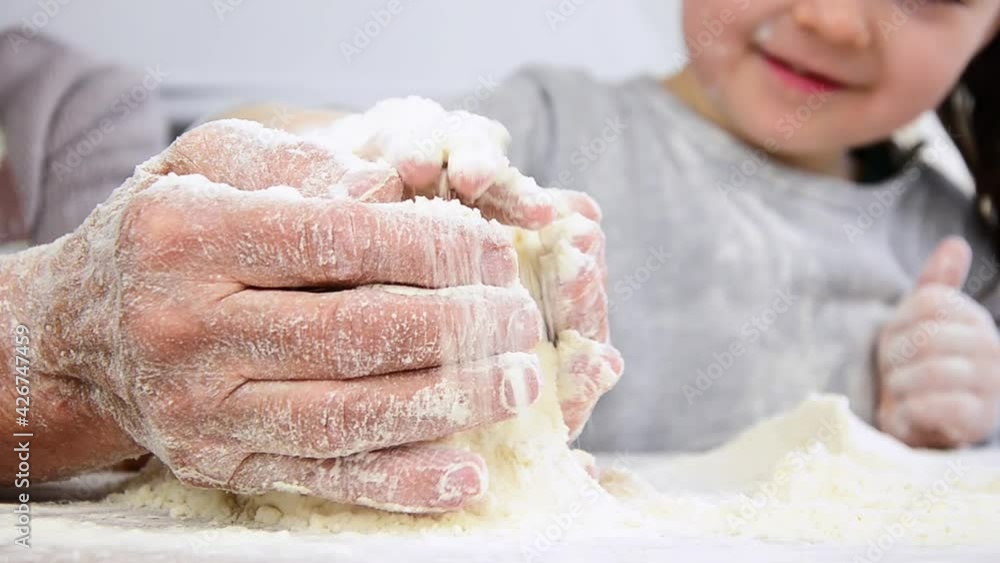 Children's hands sift flour into old palms. A grandmother with a child in flour. Grandma teaches the child to knead the dough. Old and children's hands in flour. The child holds the flour in his hands Children's hands sift flour into old palms. A grandmother with a child in flour. Grandma teaches the child to knead the dough. Old and children's hands in flour. The child holds the flour in his hands