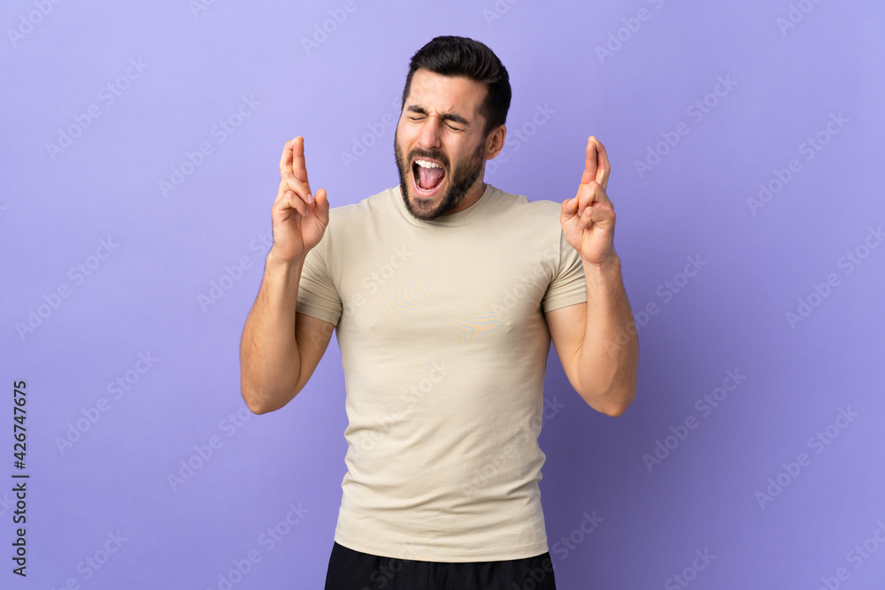 Fototapeta premium Young handsome man with beard over isolated background with fingers crossing