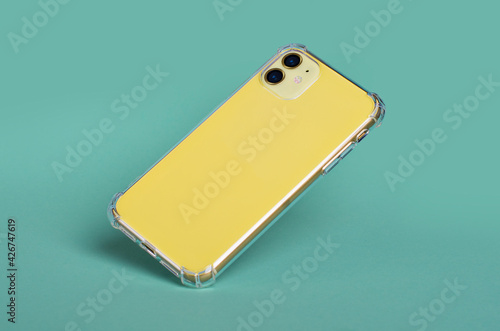 Yellow iPhone 11 in clear silicone case falls down isolated on green background back view. Phone case mockup