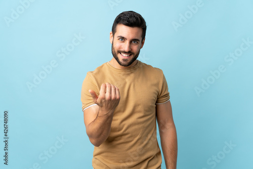 Young handsome man with beard over isolated background inviting to come with hand. Happy that you came