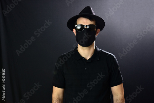 Man in hat, glasses and mask on black background.