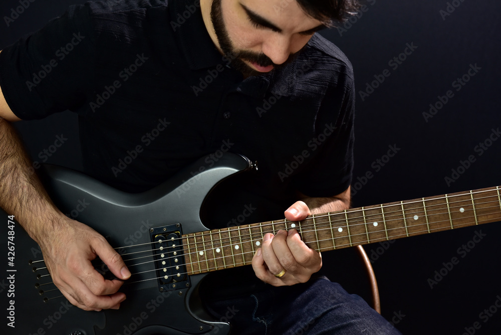 Fototapeta premium Young man playing black guitar on black background.