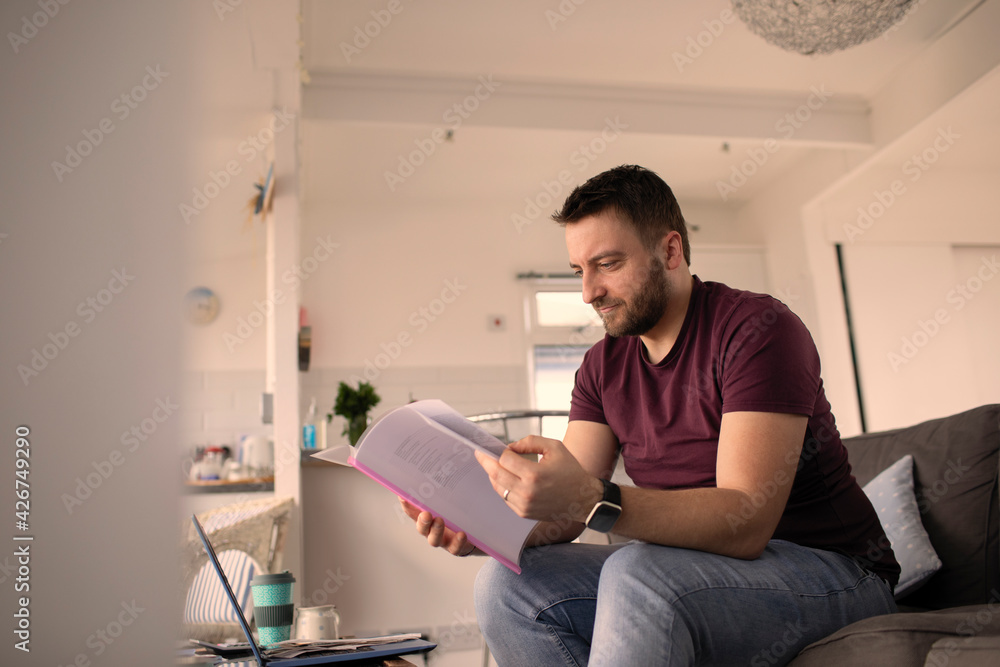 Man with paperwork working from home at laptop on sofa Man with paperwork working from home at laptop on sofa