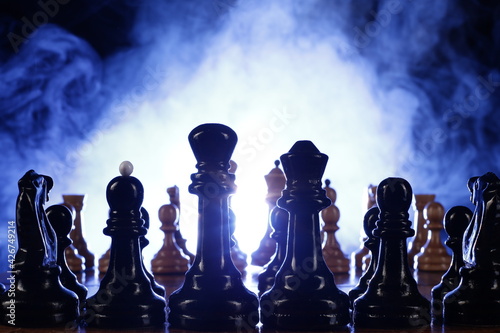 Chess is a board game. Chess pieces on a dark background in smoke