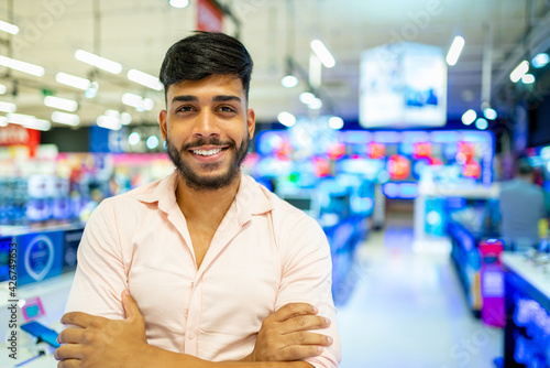 Smiling latin american man at electronics session in supermarket, looking at camera