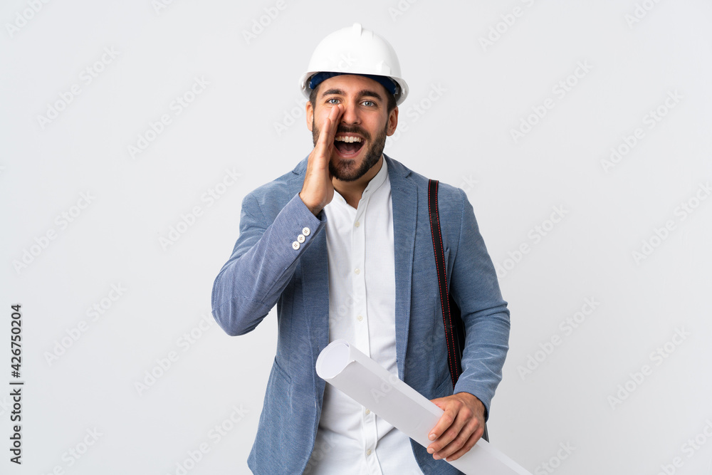 Young architect man with helmet and holding blueprints isolated on white background shouting with mouth wide open Young architect man with helmet and holding blueprints isolated on white background shouting with mouth wide open