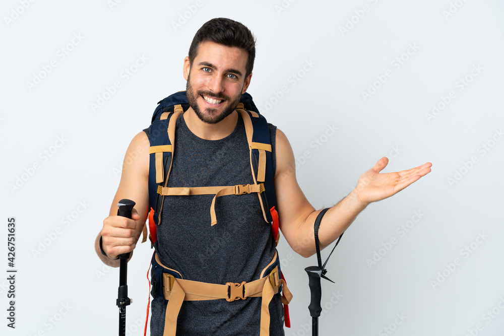 Young mountaineer man with a big backpack and trekking poles isolated on white background holding copyspace imaginary on the palm Young mountaineer man with a big backpack and trekking poles isolated on white background holding copyspace imaginary on the palm