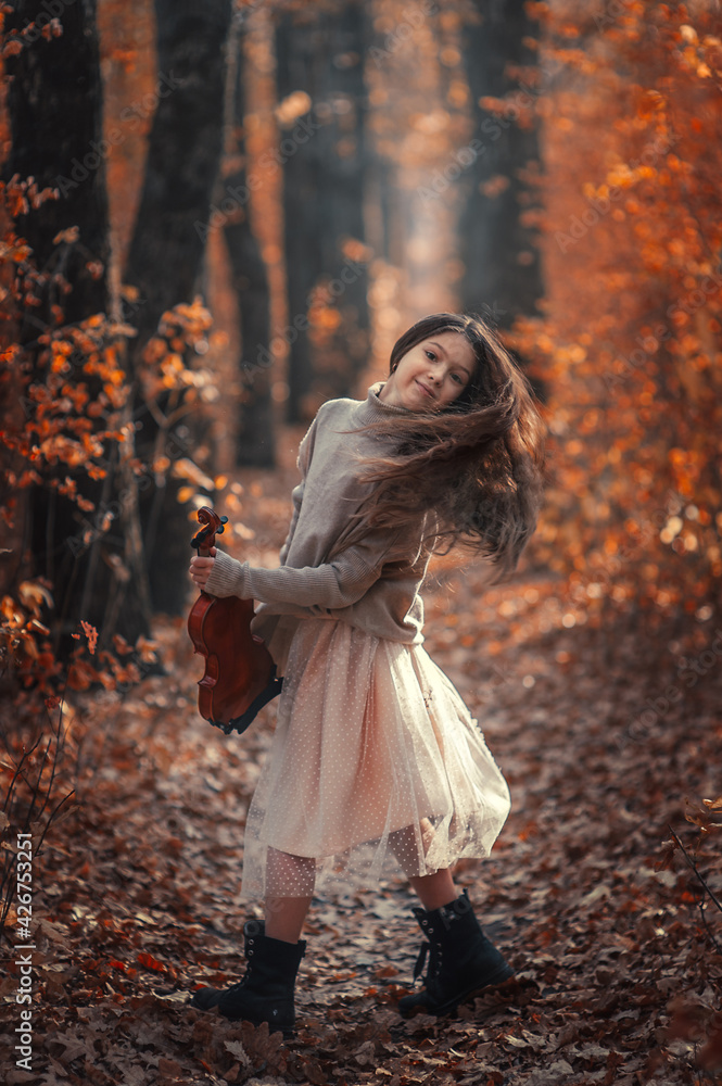 A beautiful girl with long hair plays the violin in the autumn forest.