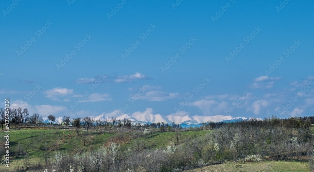 Green valleys and hills, blue sky. Mountains covered with snow in the distance. Arrival of Spring Green valleys and hills, blue sky. Mountains covered with snow in the distance. Arrival of Spring