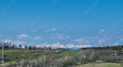 Green valleys and hills, blue sky. Mountains covered with snow in the distance. Arrival of Spring
