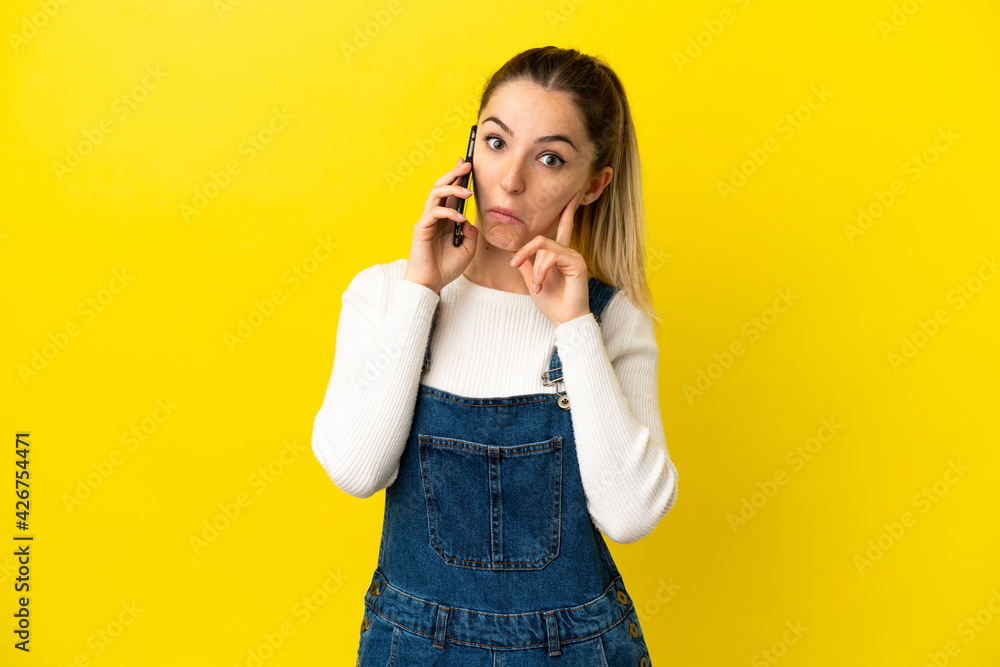 Young woman using mobile phone over isolated yellow background thinking an idea Young woman using mobile phone over isolated yellow background thinking an idea