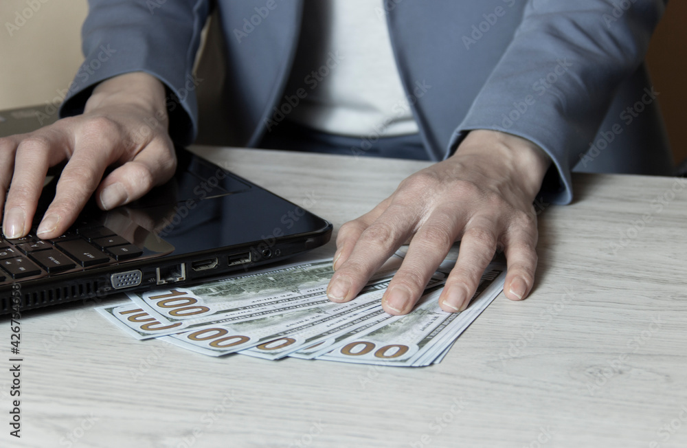 Close-up of hands shopping/paying online using laptop while holding US dollars.. Close-up of hands shopping/paying online using laptop while holding US dollars..
